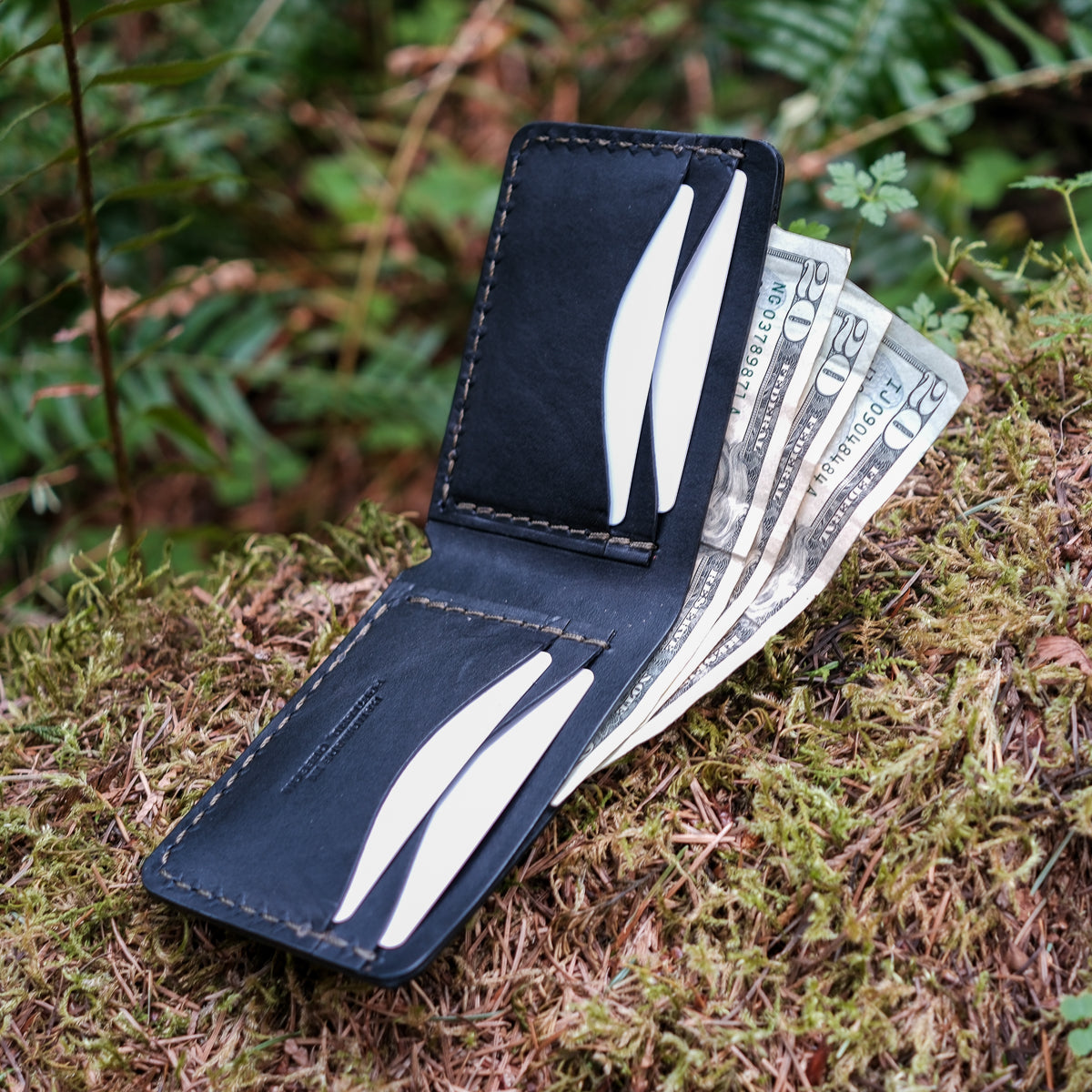 Black leather wallet with money on a mossy surface