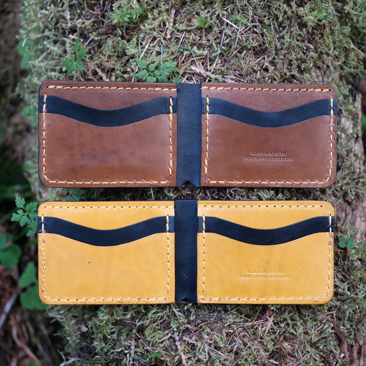 Two leather card holders, one brown and one yellow, on a mossy background.